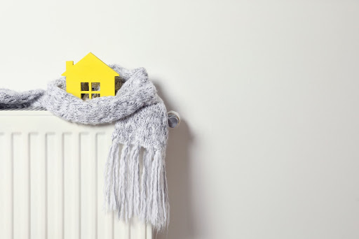 A small wooden house wrapped in a scarf on top of a radiator.