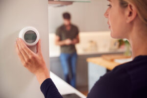 A woman adjusting a thermostat to reduce heating costs in a Hagerstown, MD, home.