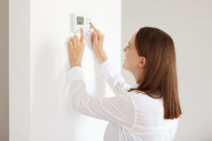 A smiling woman adjusting a thermostat on a white wall.