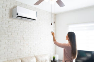 A woman turning on a ductless HVAC unit with a remote inside a home.