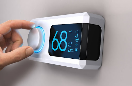 Hand adjusting smart thermostat that reads 68 degrees Fahrenheit.