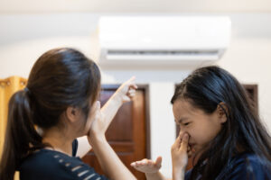 Two women holding their nose while pointing at AC for smelling bad.